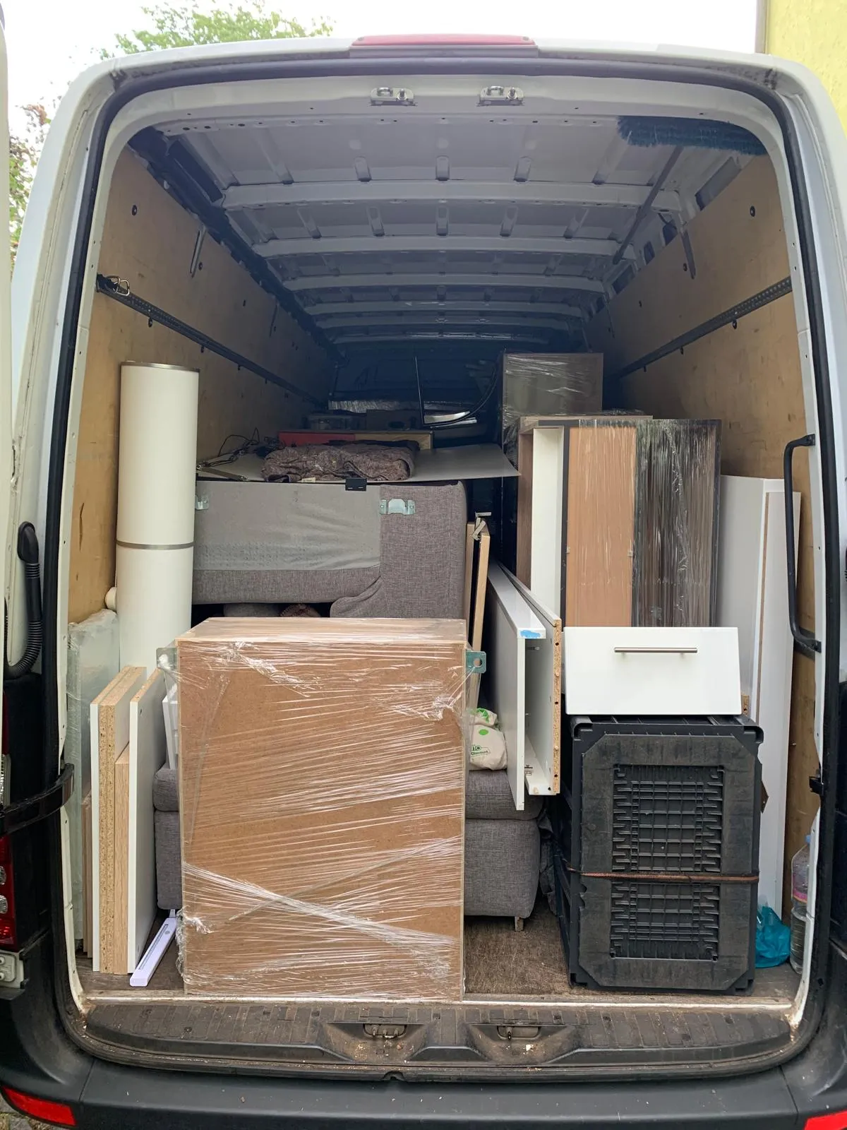 Rückseite eines Lieferwagens offen und voll mit verpackten Möbelstücken und Holzteilen.
